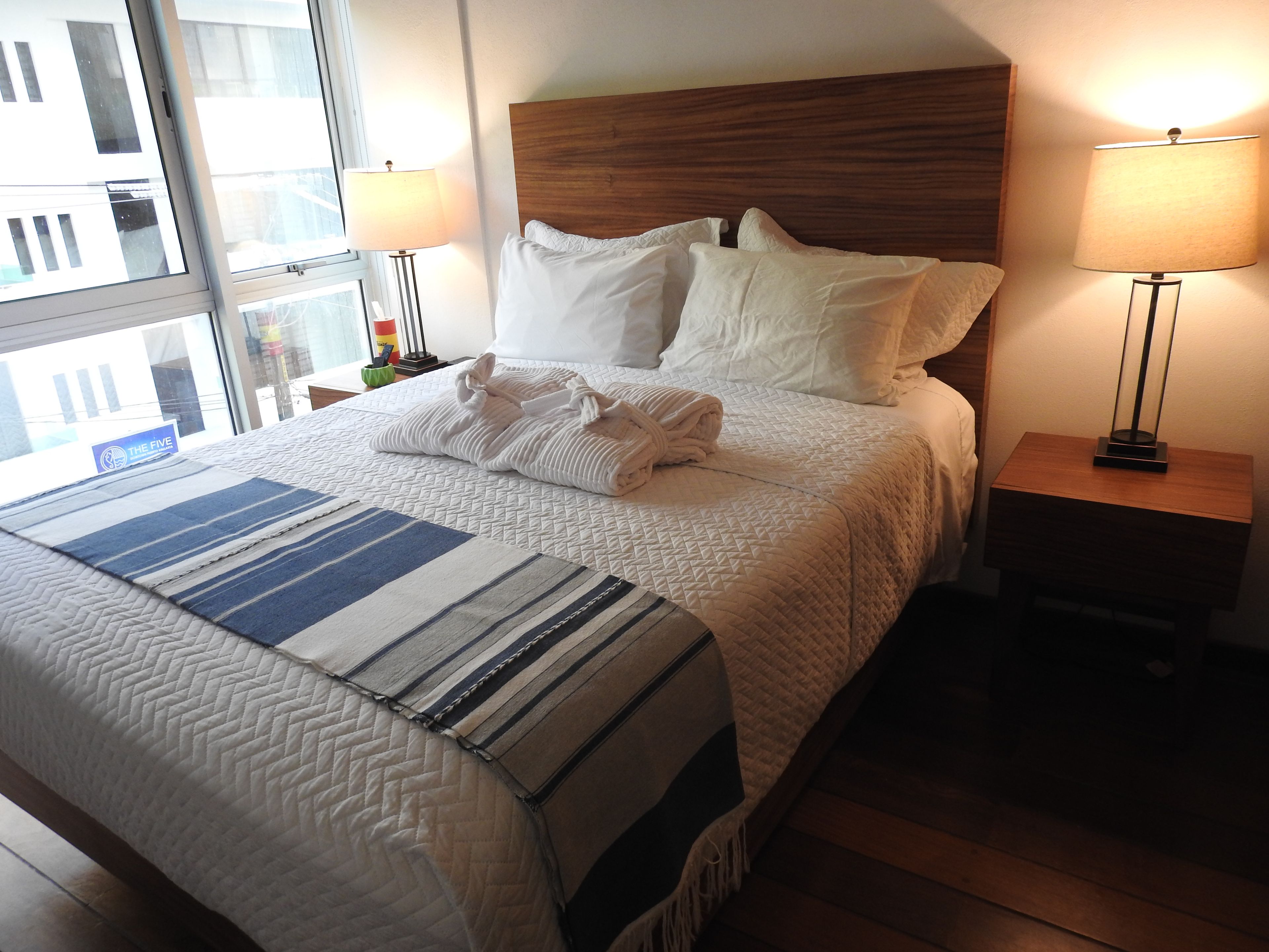 A hotel room with a large bed, two bedside lamps, a window with a view, and a striped throw blanket.
