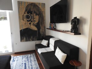 A living room with a black sofa, white cushions, a blue patterned rug, a coffee machine, and a large painting on the wall. - AVA19 Adults Only Villa (Puerto Vallarta)