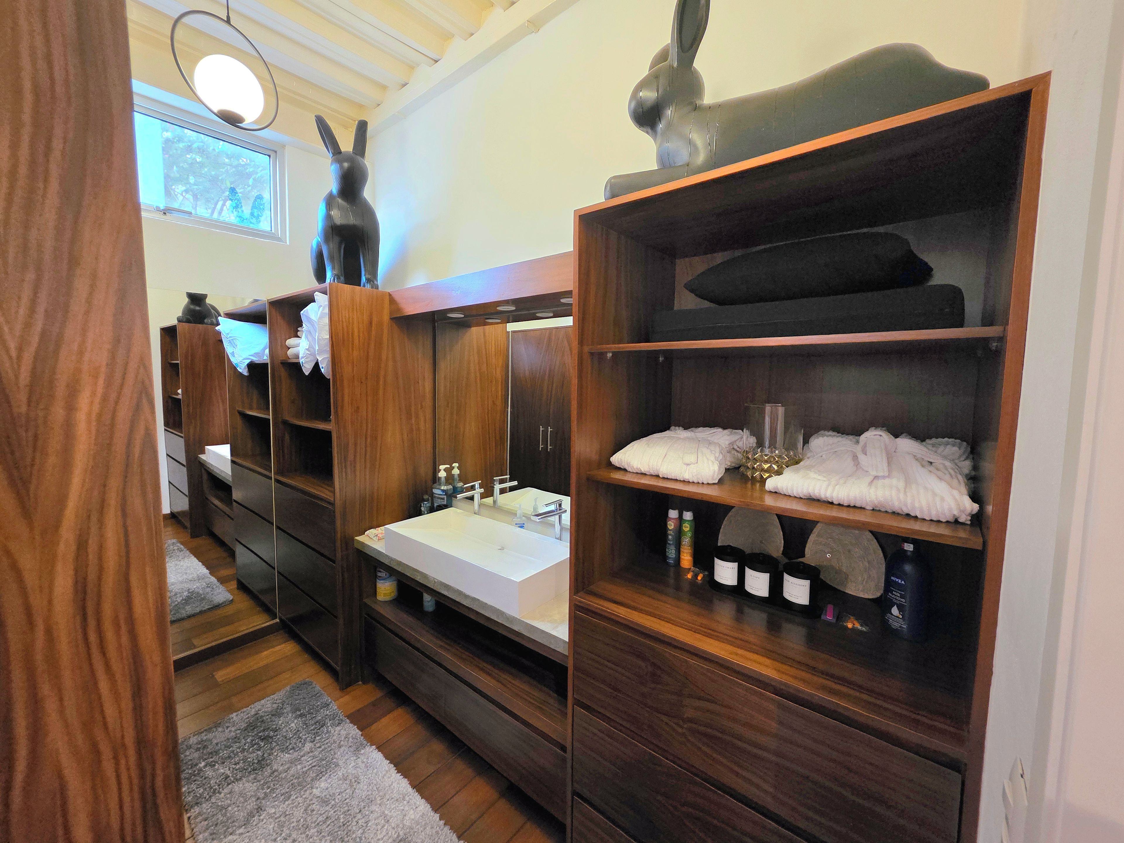 A modern bathroom with a wooden vanity, a large mirror, and a shelf with toiletries.