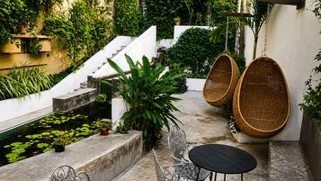 A patio with a small pool, wicker chairs, a table, and a staircase leading to a higher level.