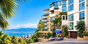 A multi-story hotel with balconies, a view of the sea, and parked cars. - AVA19 Adults Only Villa (Puerto Vallarta)