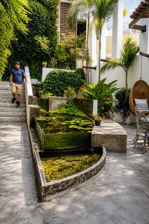 A man walking on a tiled staircase, a small pond with lily pads, and a wicker chair. - AVA19 Adults Only Villa (Puerto Vallarta)
