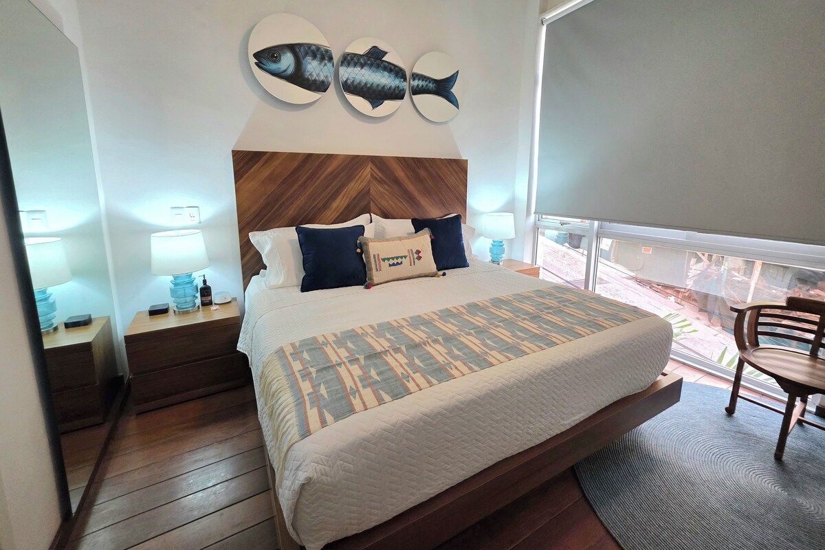 A hotel room with a bed, nightstands, a wooden headboard, two wall-mounted fish decorations, a window with a view, and a balcony with a chair.