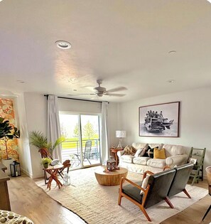 Un salon spacieux doté d’un ventilateur de plafond, d’un ensemble de canapés, d’une table basse et d’un coin repas avec des chaises et une table.