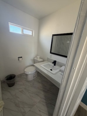 A bathroom with a toilet, sink, and a small window. - deluxe motel (Pomona)