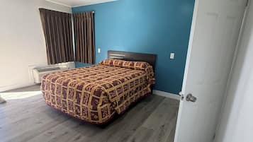 A bedroom with a bed, a window with curtains, a door, and a ceiling with recessed lighting.