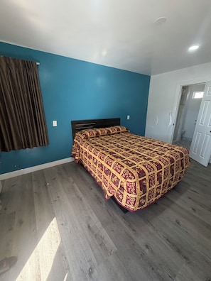 A bedroom with a bed, a door, and a blue wall. - deluxe motel (Pomona)