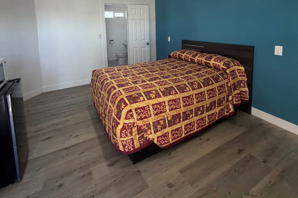 A bedroom with a bed, a dresser, and a door leading to a bathroom.