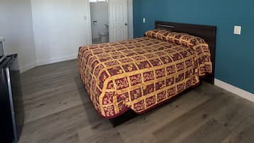 A bedroom with a bed, a dresser, and a door leading to a bathroom.
