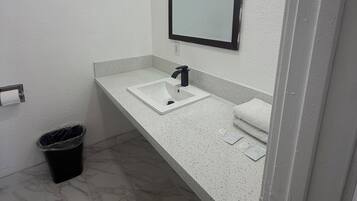 Un baño con un lavamanos blanco, un espejo y un cubo de basura negro.
