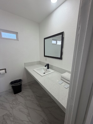 A bathroom with a white sink, a mirror, and a black trash bin. - deluxe motel (Pomona)