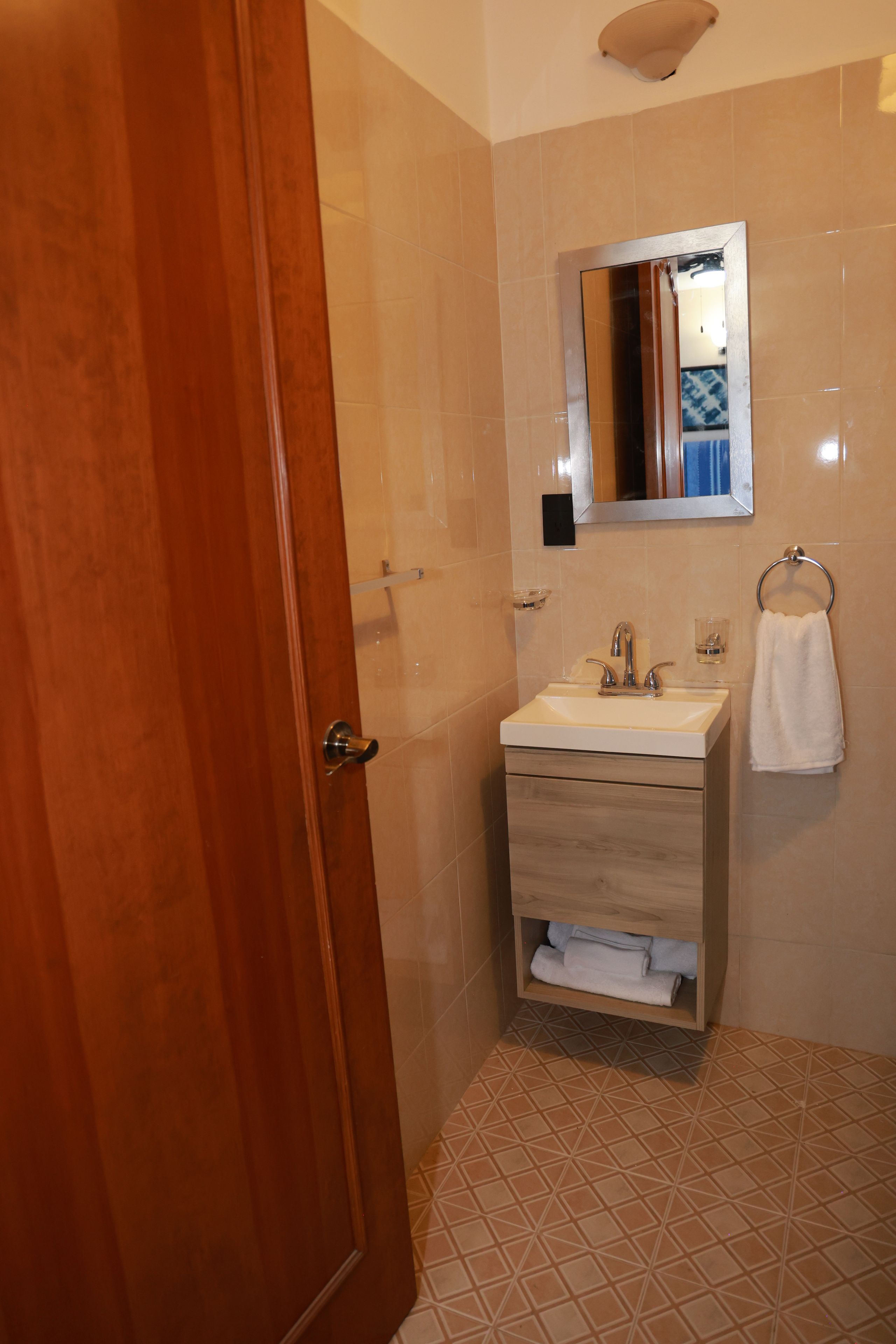 A bathroom with a wooden door, a sink with a mirror above it, and a towel rack.