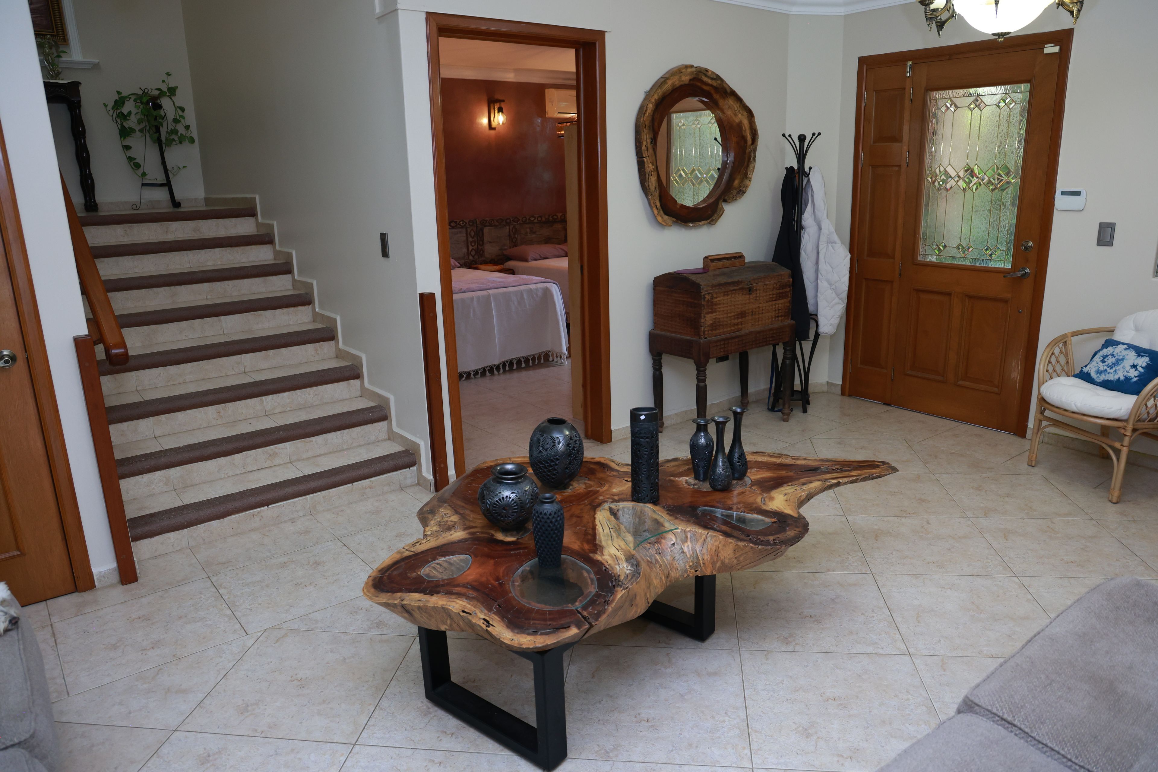 Una sala de estar con una mesa de centro de madera, una escalera, una puerta con panel de vidrio y una silla.