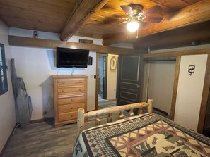 Ein Schlafzimmer mit einem Bett, einer Holzkommode, einem Fernseher, einem Deckenventilator und einer Tür.