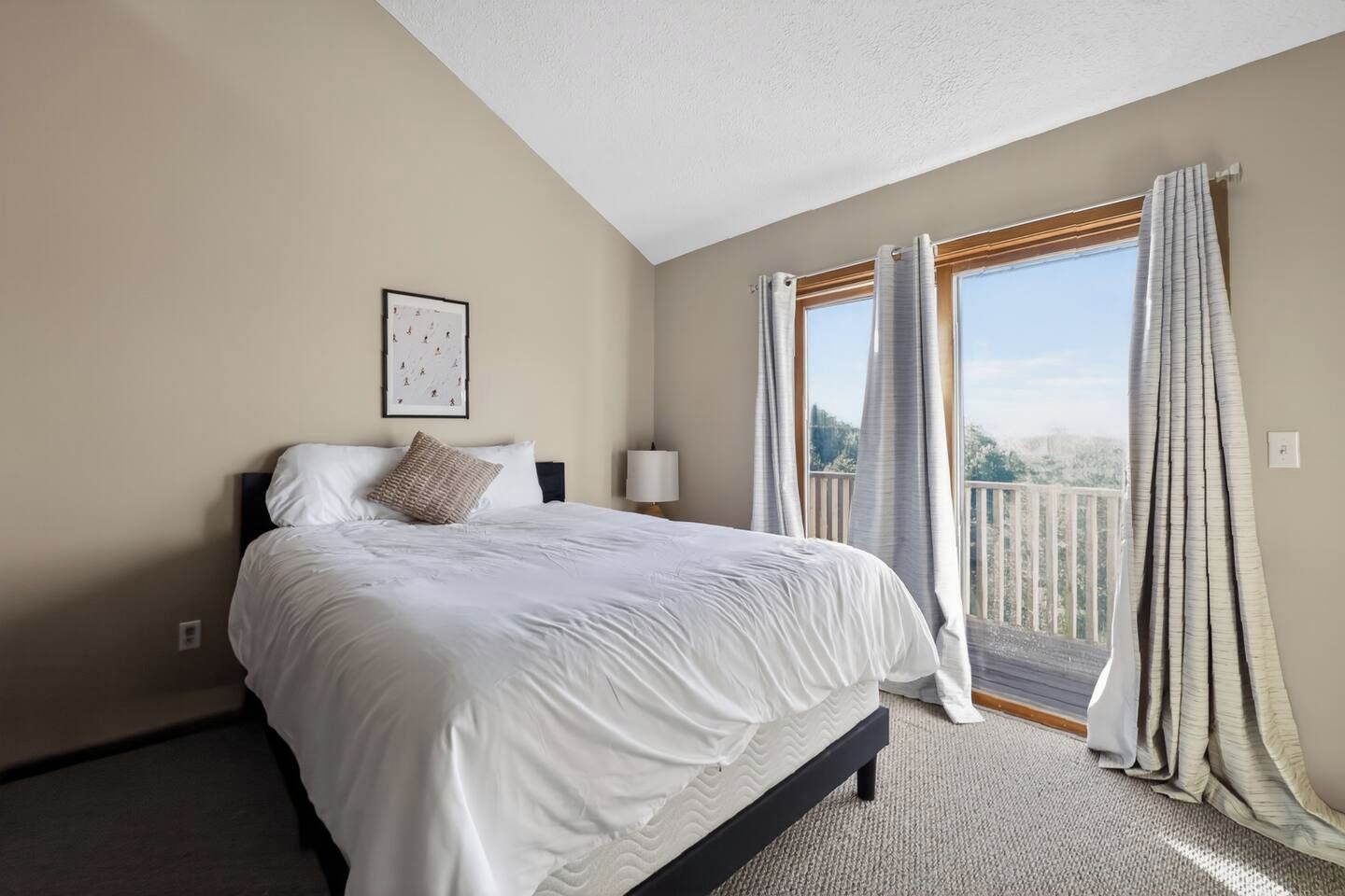 A hotel room with a bed, a nightstand, a lamp, and a window with curtains.