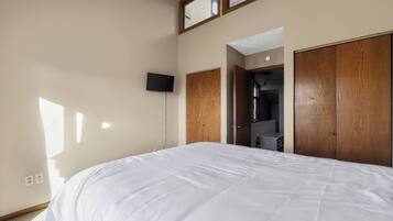 Ein Schlafzimmer mit einem großen Bett, einem flachbildfernseher an der Wand und einem Holzschrank.