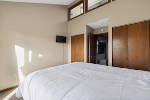A bedroom with a large bed, a flat-screen TV mounted on the wall, and a wooden wardrobe. - 3BR Otsego Condo|Ski, Golf & Sturgeon Valley Views (Gaylord)