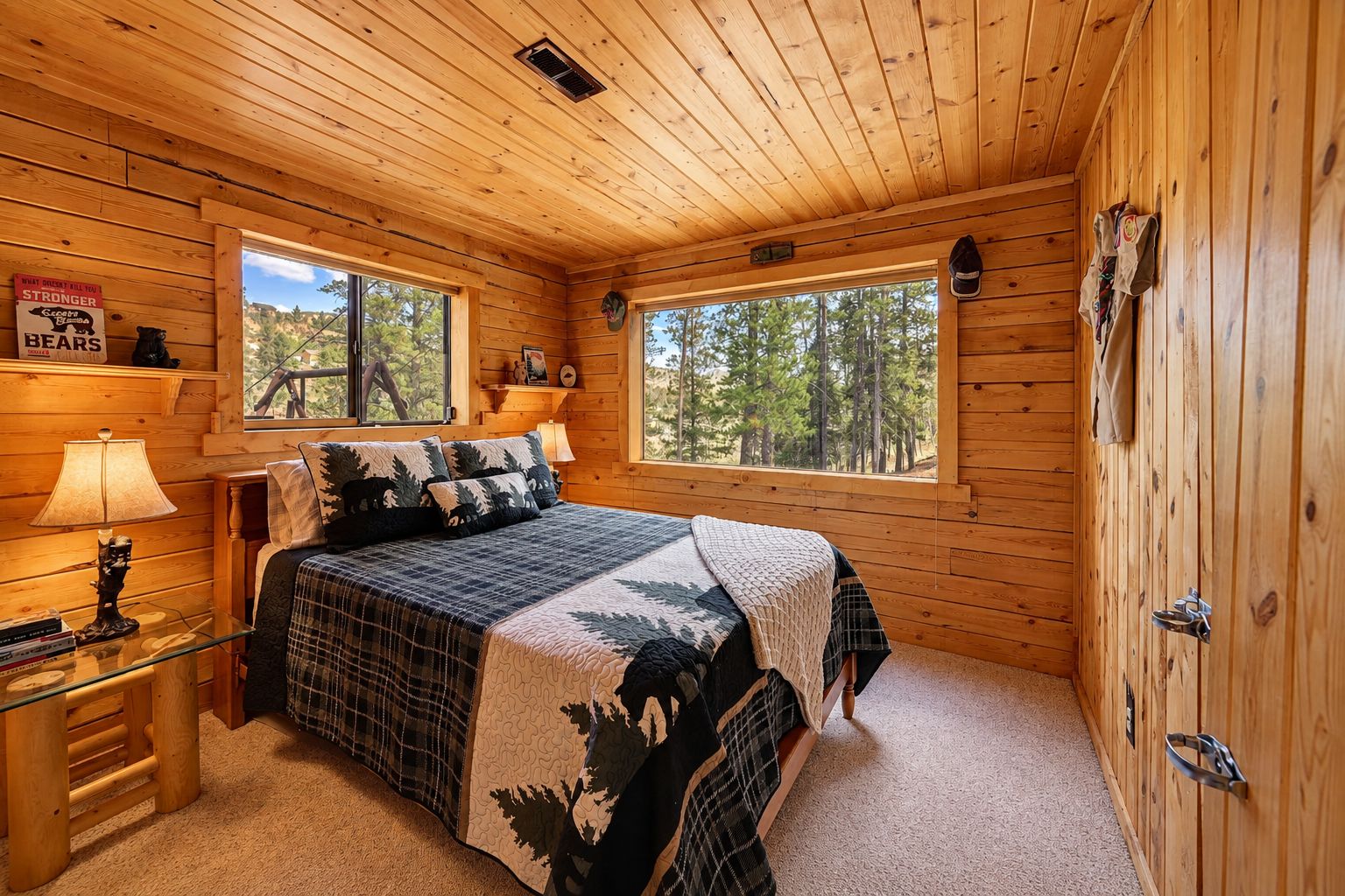 A wooden cabin bedroom with a bed, two windows, a nightstand, and a dresser.