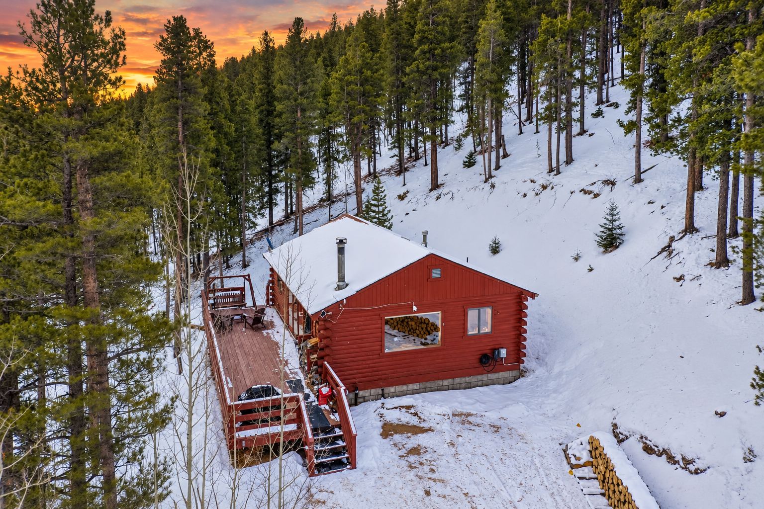 Une cabane rouge avec une terrasse, entourée d’arbres et de neige.