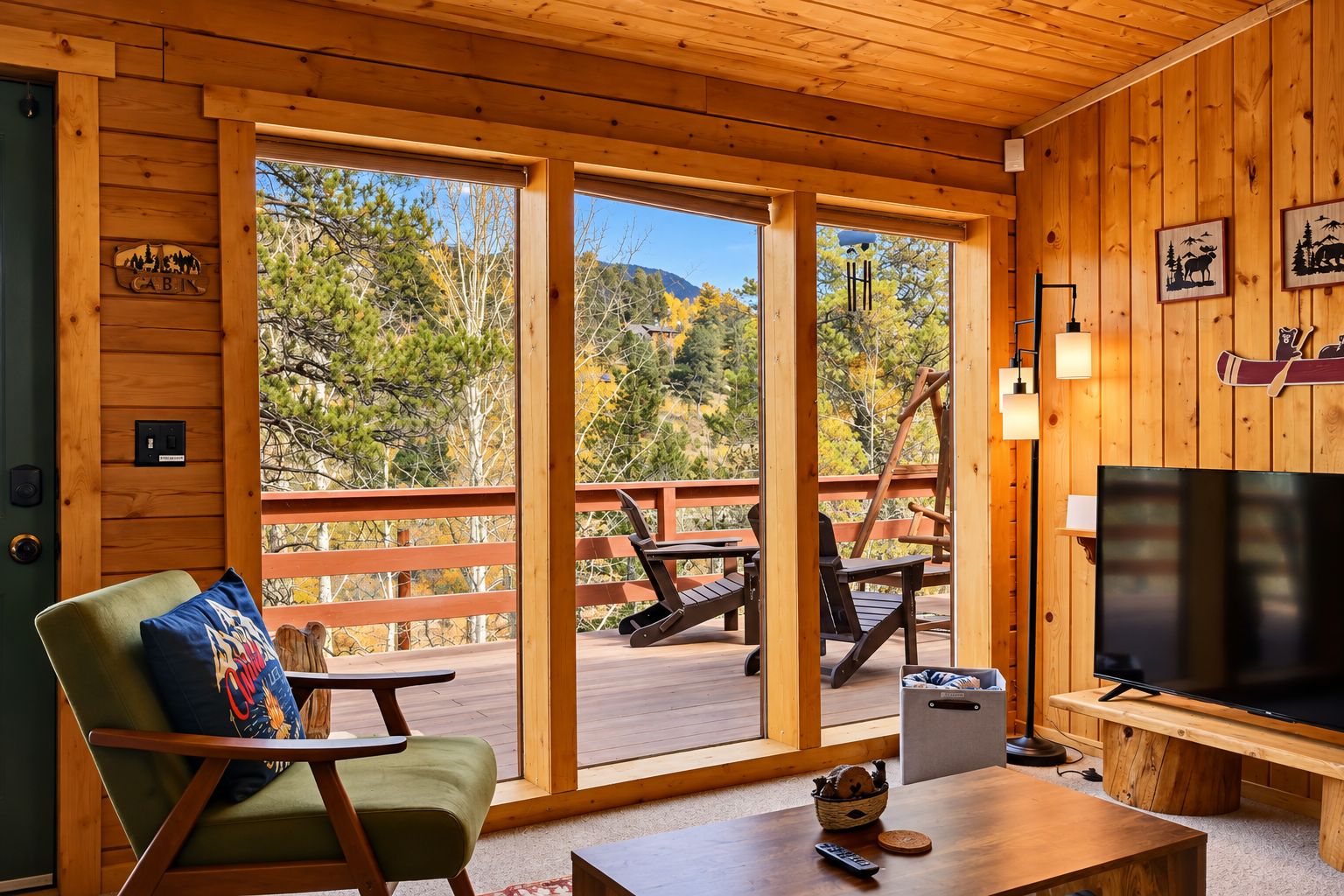 L'intérieur d'un chalet est aménagé avec un grand téléviseur, des meubles en bois et offre une vue sur les arbres et les montagnes par les fenêtres.