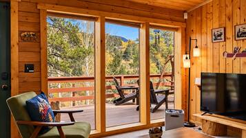 L'intérieur d'un chalet est aménagé avec un grand téléviseur, des meubles en bois et offre une vue sur les arbres et les montagnes par les fenêtres.