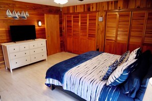 A bedroom with a bed, dresser, and a television on a wooden wall. - Paddle Point Retreat - Mountain & Lake Views - Fire Pit (McHenry)