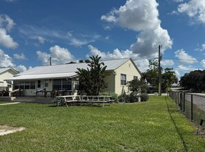 Um imóvel residencial com jardim frontal, mesa de piquenique e área cercada.
