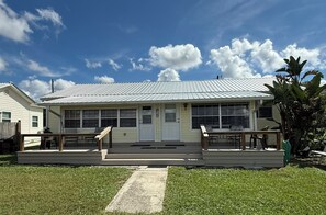 Um edifício térreo com telhado plano, varanda frontal com banco e um pequeno jardim.