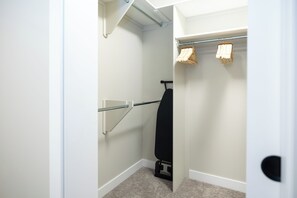 A walk-in closet with a hanging rod, a shoe rack, and a door leading to another room. - Hebron Place | Elegant 3-Bedroom Stay for 6 (Regina)