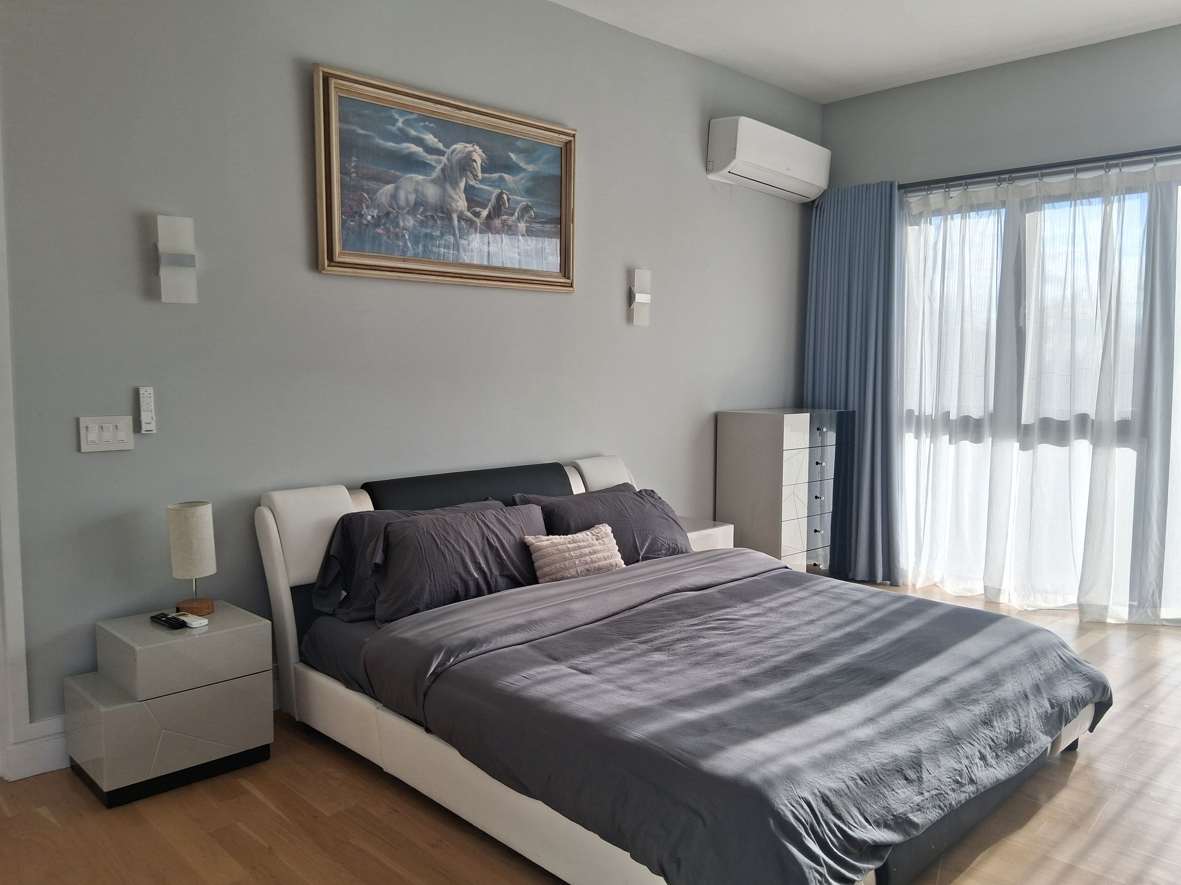 Ein modernes Schlafzimmer mit Bett, Nachttischen, einem Schrank, einem Gemälde und einer Klimaanlage.