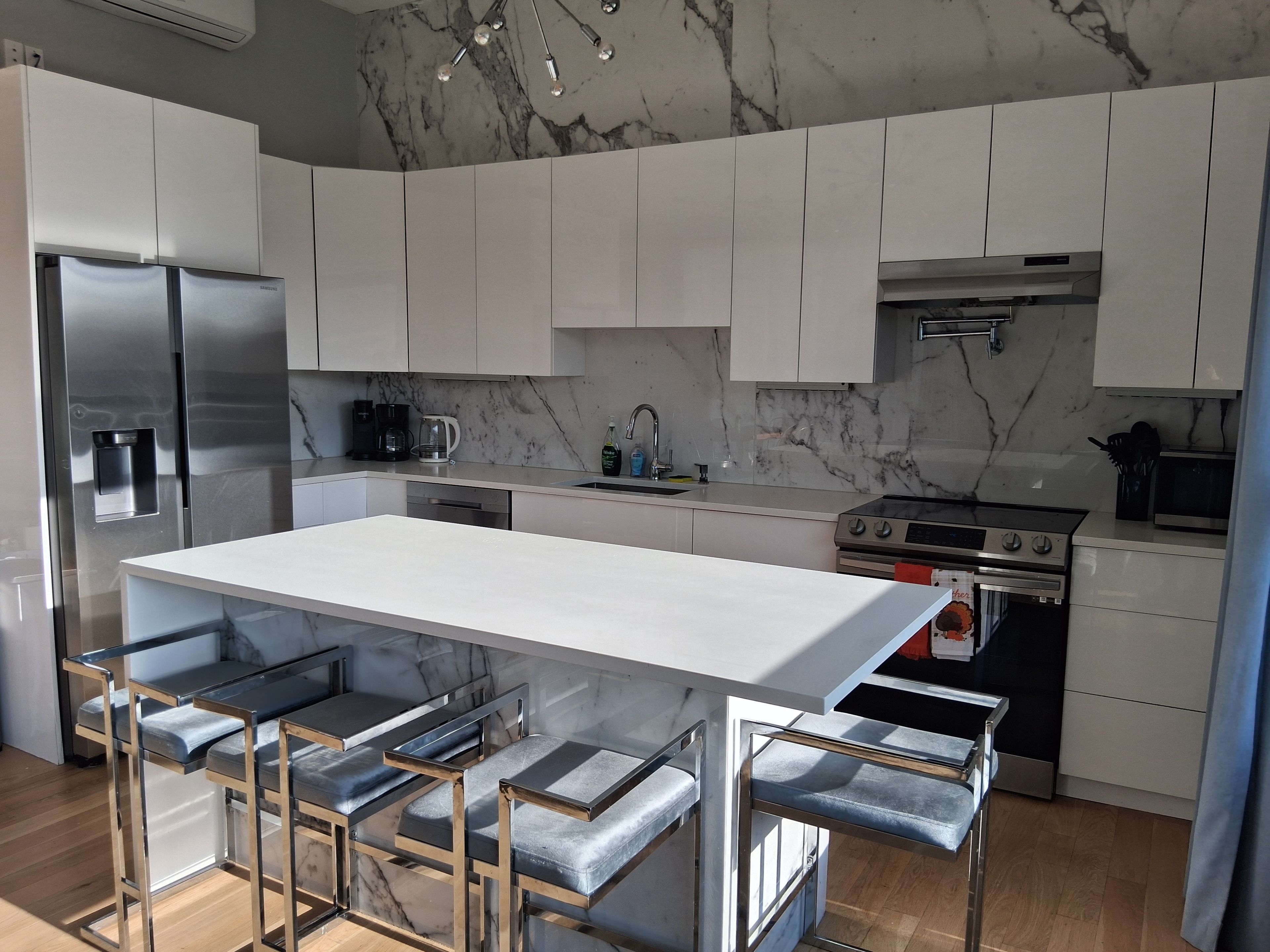 A modern kitchen with white cabinets, a stainless steel refrigerator, a gas stove, and a marble backsplash.