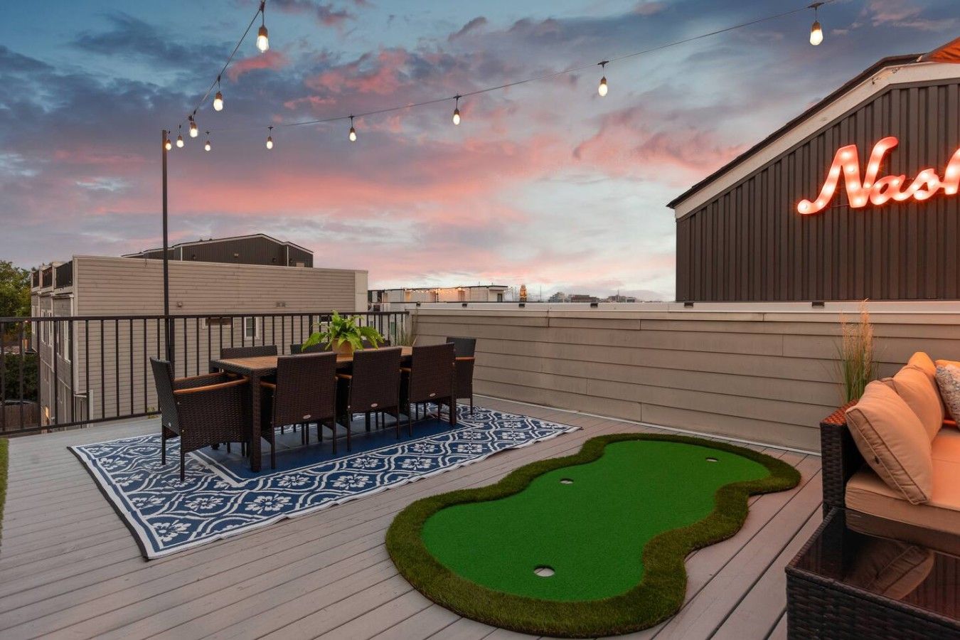 Une terrasse sur le toit aménagée avec un coin repas, un putting green et des guirlandes lumineuses.