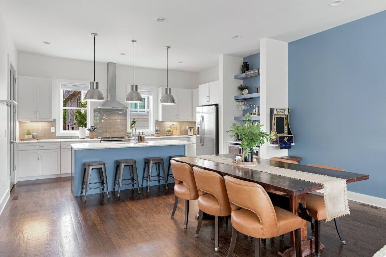 A modern kitchen with a central island, bar stools, pendant lighting, and a blue accent wall.