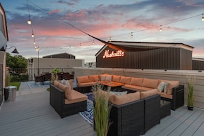 En tagterrasse med udendørs møbler, lyskæder og et neonskilt.