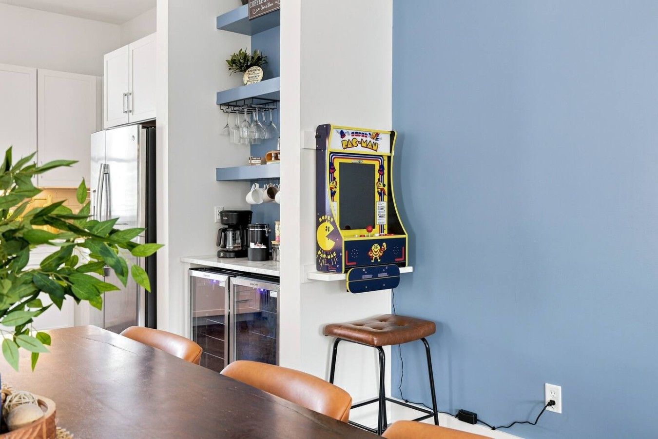 Une cuisine équipée d’une machine à café, d’un réfrigérateur et d’une borne d’arcade fixée au mur.