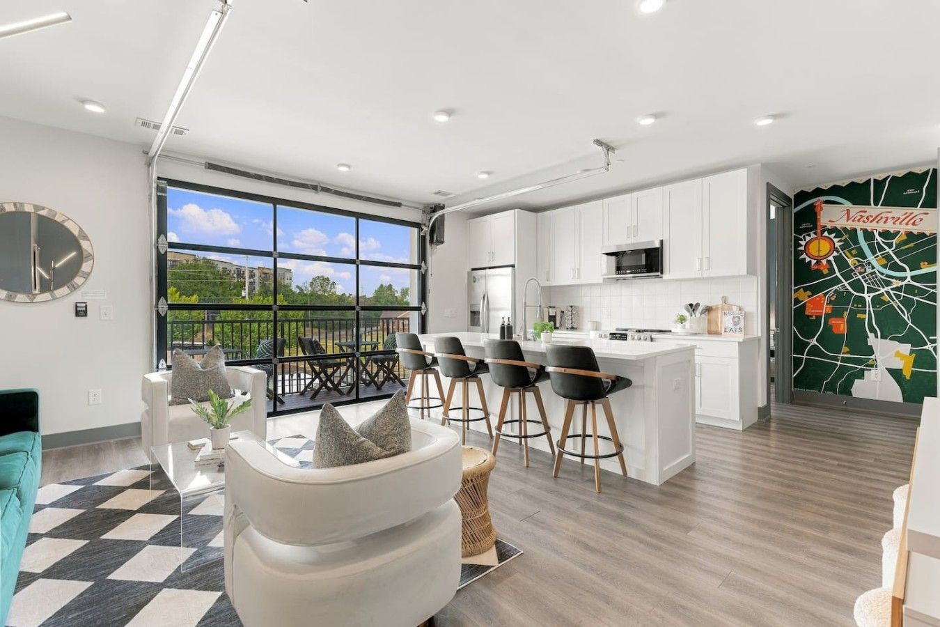 A modern kitchen with white cabinets, a central island, and a large window offering a view of greenery.
