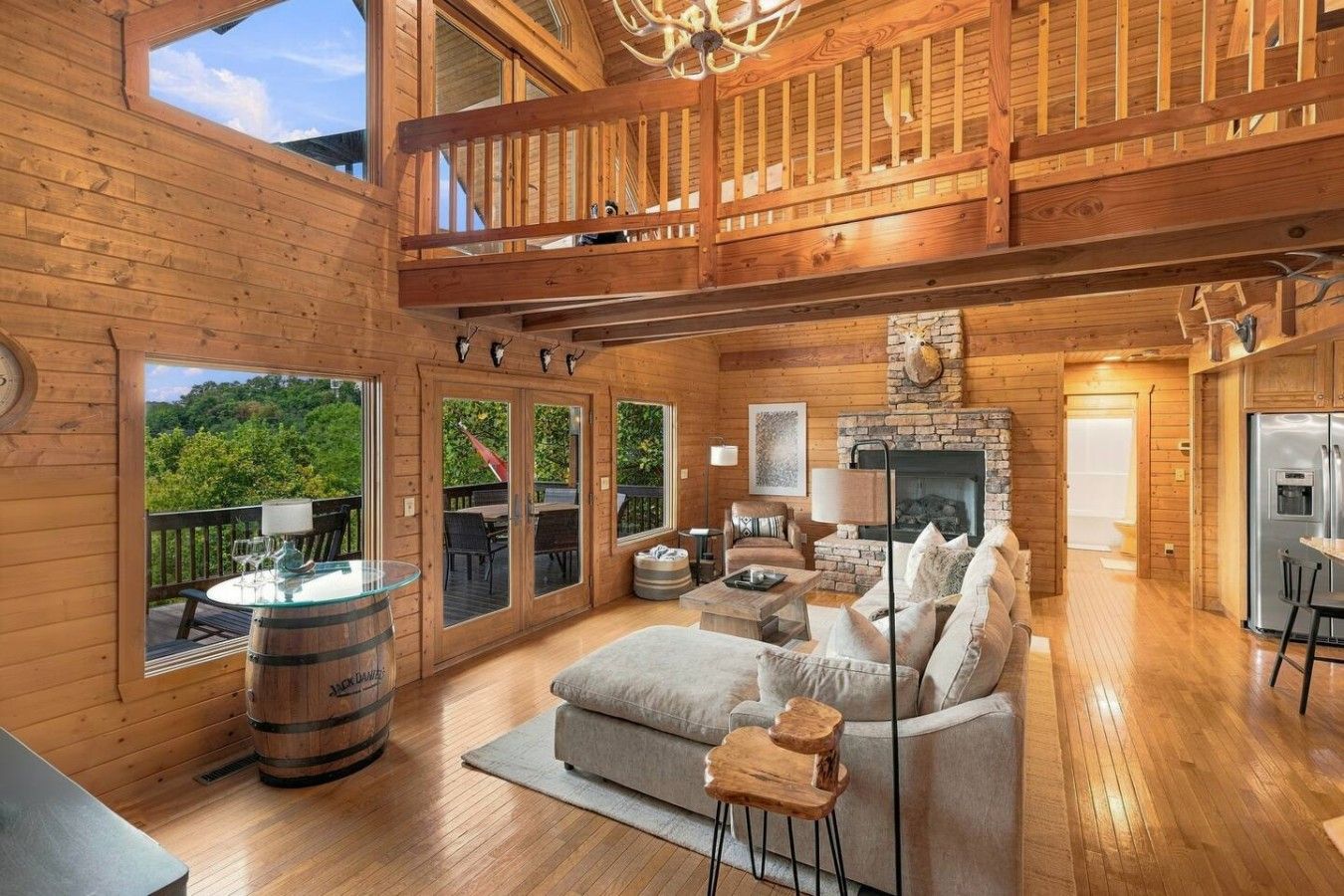 Een ruim houten interieur met een open haard, zithoek en een balkon met uitzicht op groen.
