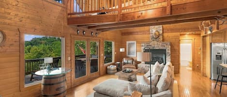A spacious wooden interior with a fireplace, seating area, and a balcony with a view of greenery.