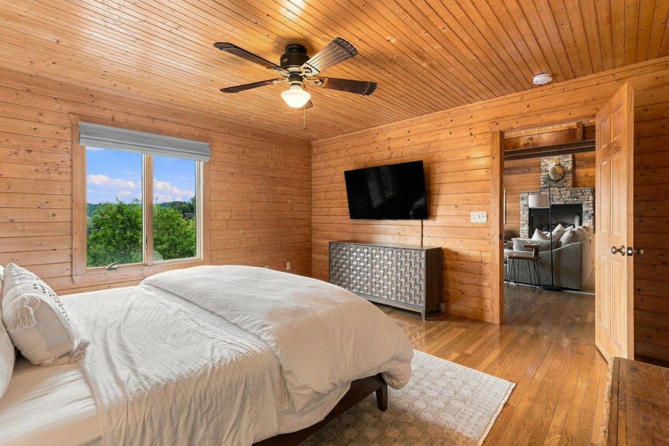 A bedroom with a bed, a television, a fireplace, and a view of the outdoors.
