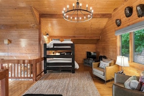Een houten blokhut van binnen met een stapelbed, een televisie, een bank en een kroonluchter.