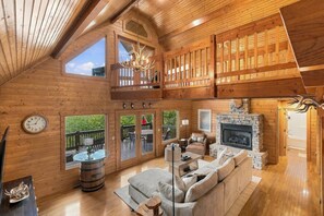 A spacious wooden cabin with a loft bedroom, a fireplace, and a large window overlooking the outdoors. - Lake Views with Hot Tub, Large Deck, Gym, Ping Pong (Smithville)