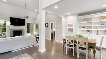 A spacious living area with a fireplace, a dining table with chairs, and a kitchen in the background.