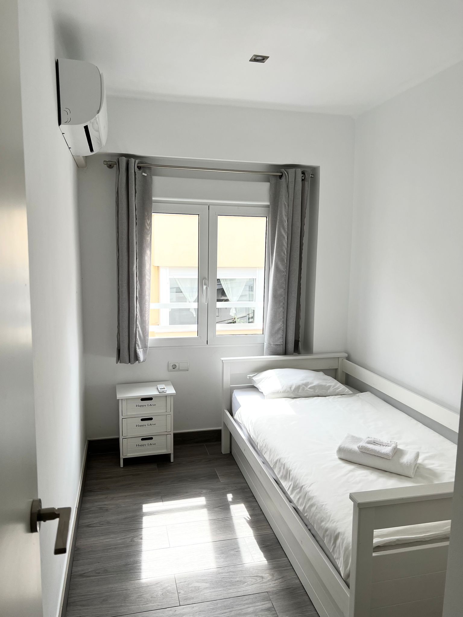 A bedroom with a single bed, a bedside table, a nightstand, and a window with curtains.