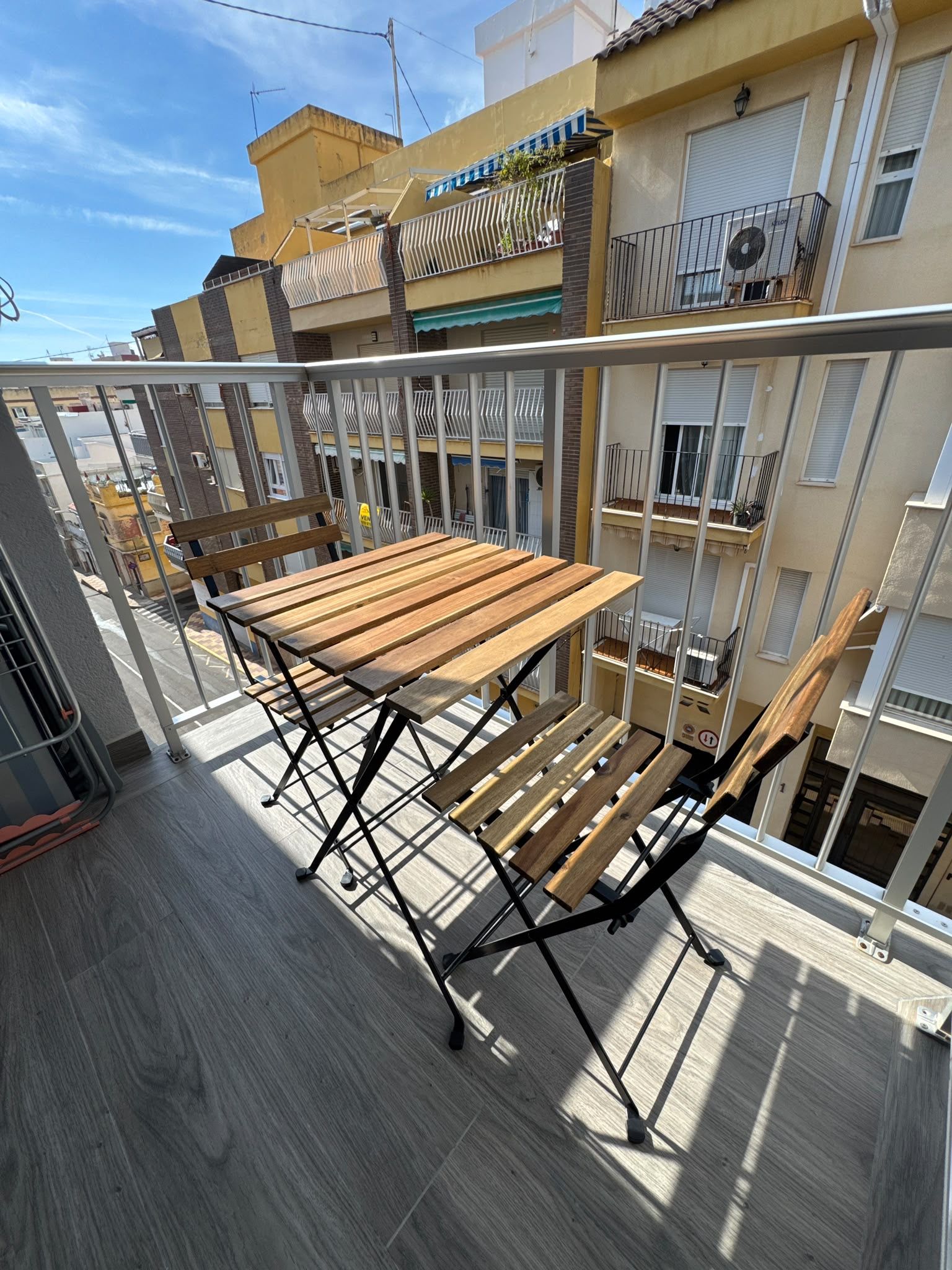 A balcony with a wooden table and chairs, overlooking a residential area with multiple buildings.