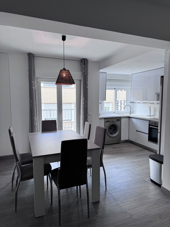 A modern kitchen with a built-in washing machine, a dining area with a table and chairs, and a hanging pendant light.