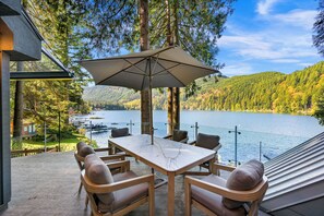 Una terraza con mesa y sillas, con vistas a un lago y colinas boscosas.