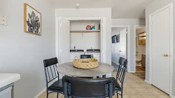 Een eethoek met een ronde tafel, vier stoelen, een rieten mand en een keuken op de achtergrond.