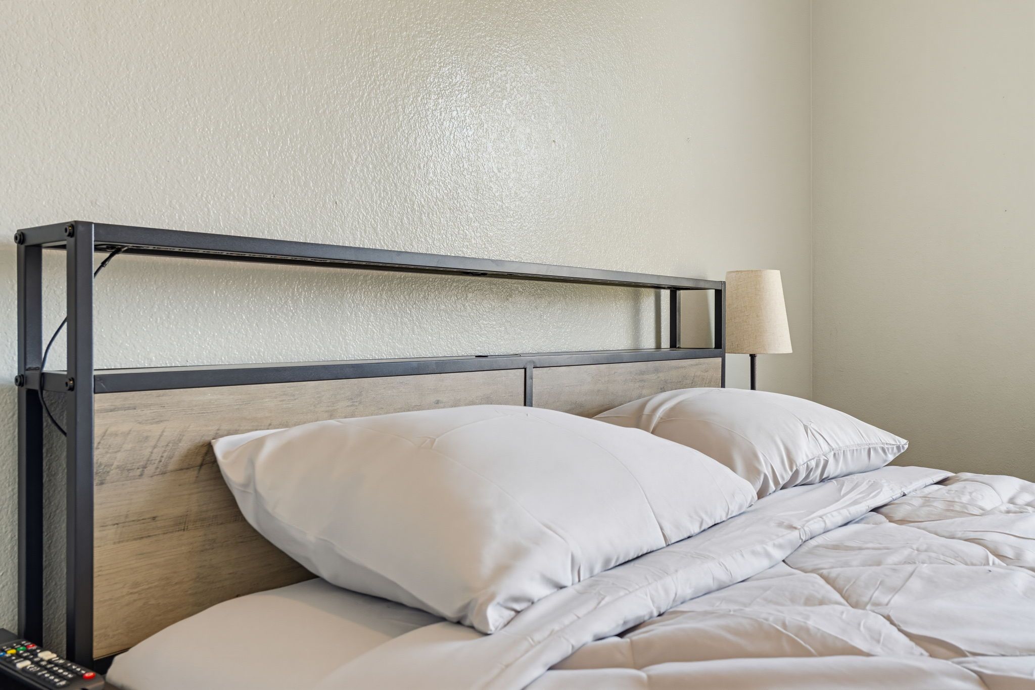 Una cama con cabecera de metal, ropa de cama blanca y una lámpara de noche.