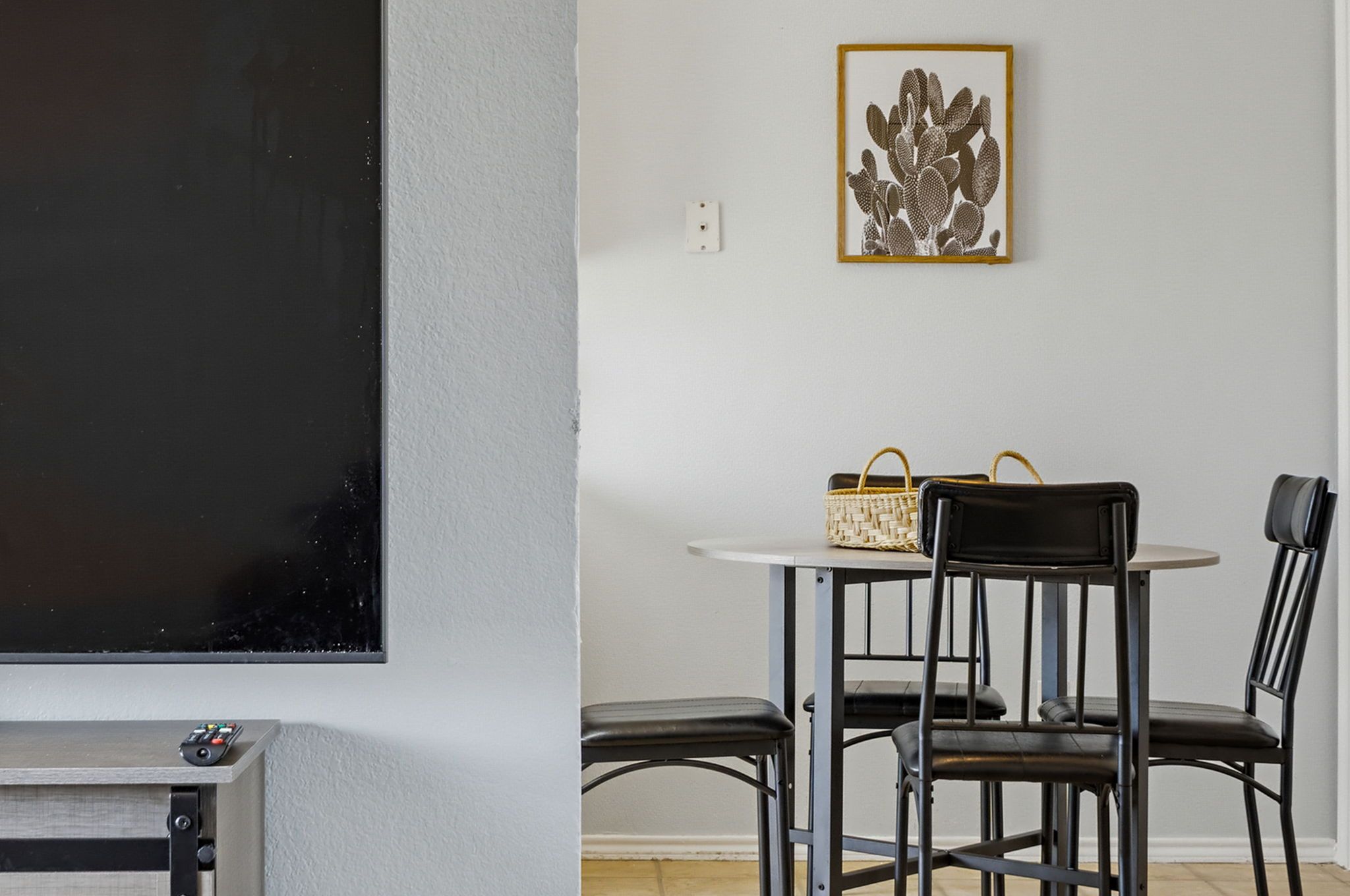 Una habitación con una pizarra, una mesa con sillas, una cesta y un cuadro enmarcado en la pared.