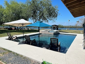 A swimming pool with lounge chairs and umbrellas, surrounded by a deck and a view of a lake. - Spacious 4bedroom Coastal CC River retreat with private pool & boardwalk fishing (Corpus Christi)